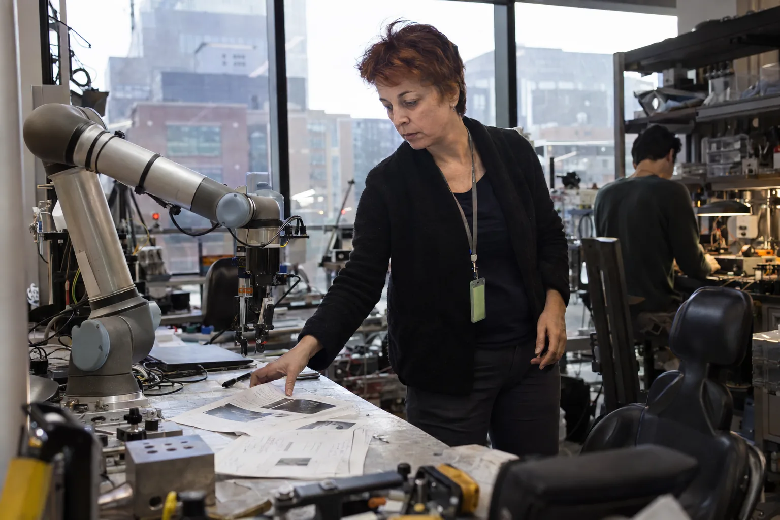 Researcher checking printed preprint pages beside a robot arm in a Cambridge lab