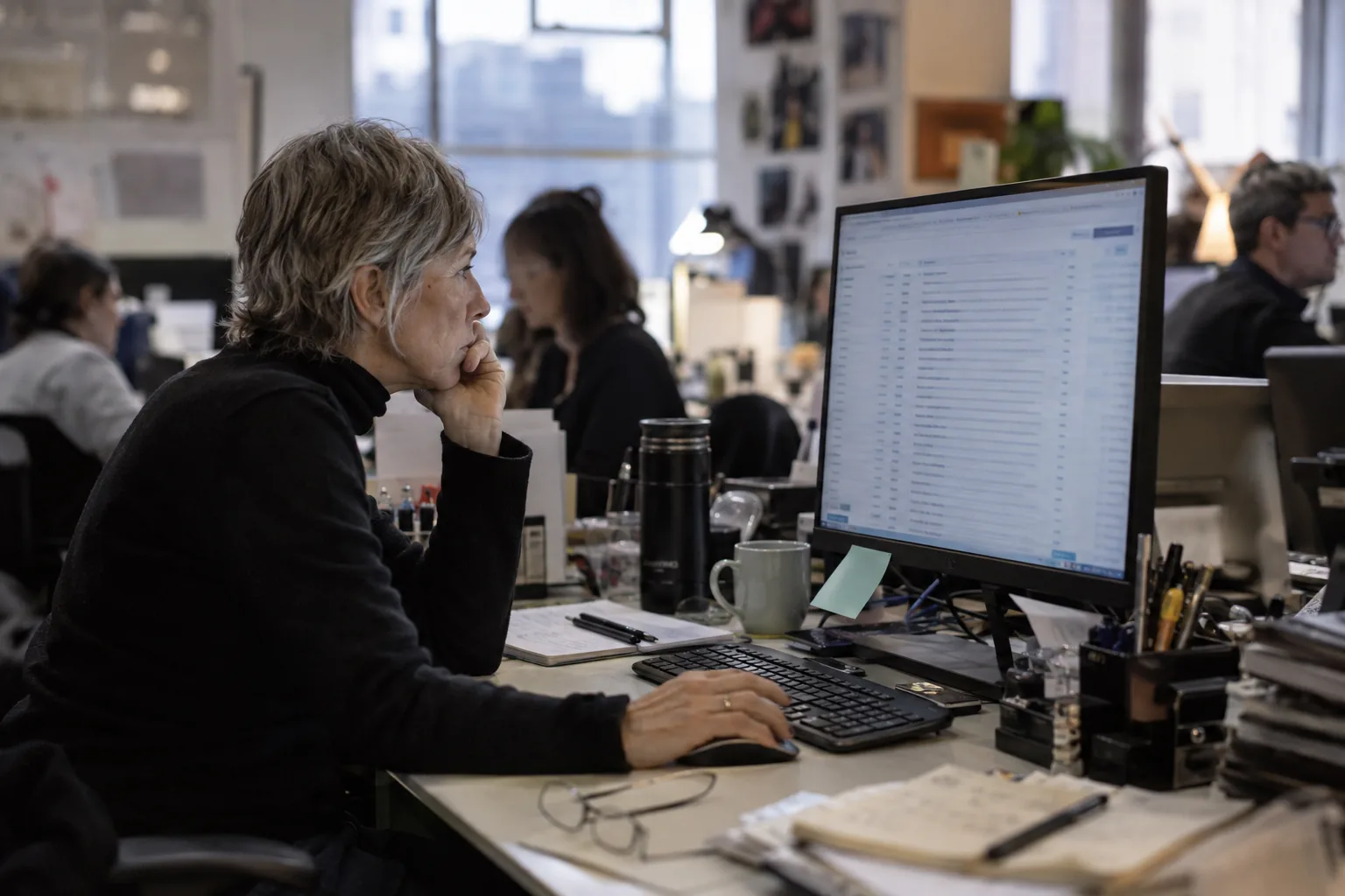 Reporter scanning a full inbox of pitches on a monitor in a busy newsroom