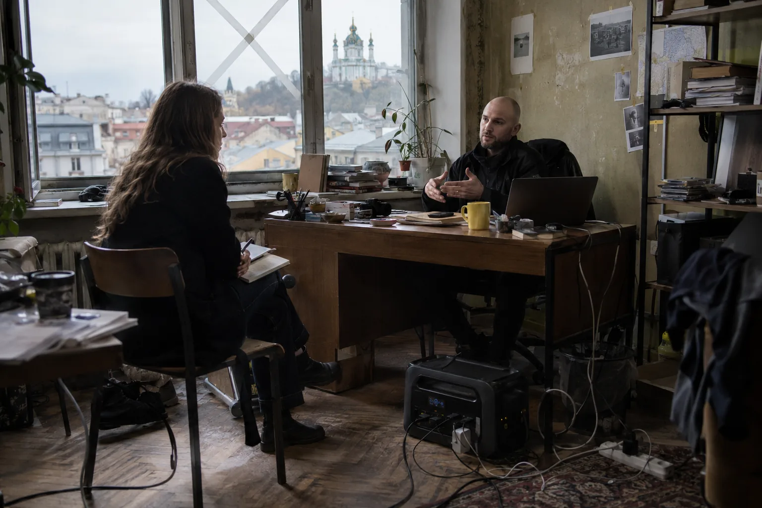 Reporter interviewing a founder in a Kyiv office, a power station on the floor and Podil outside