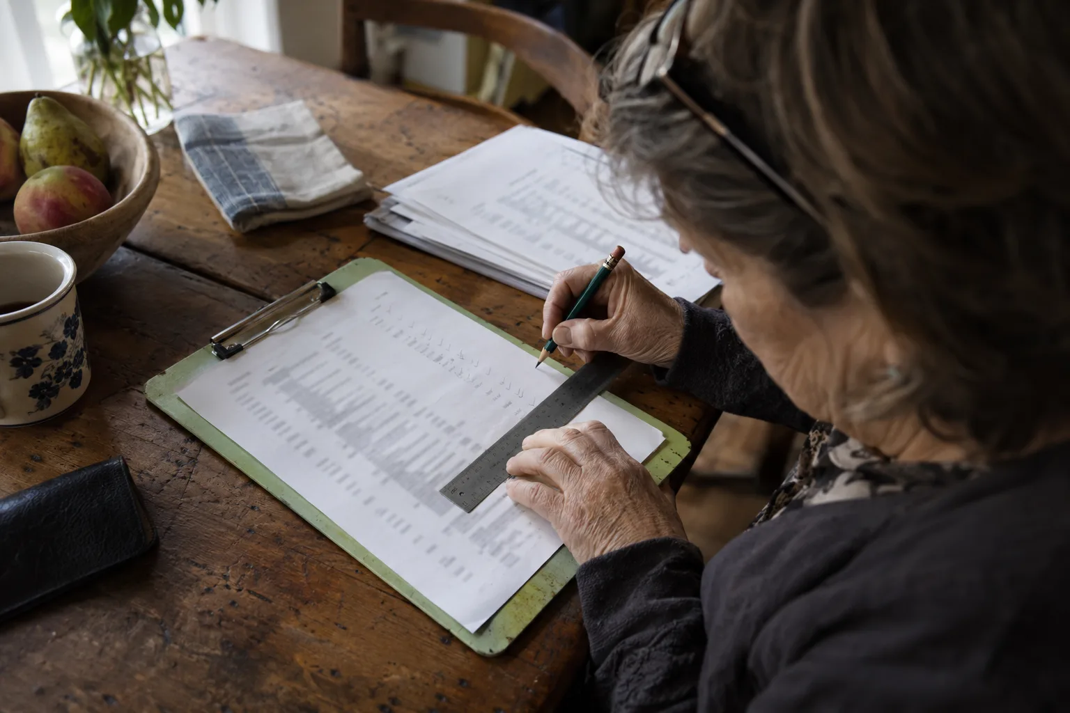 Older woman checking a fact sheet line by line with a steel ruler
