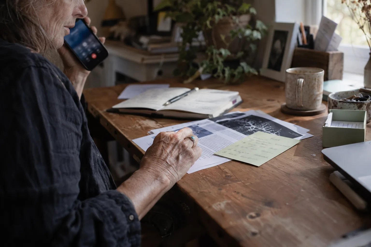 Older PR consultant on a call, her hand on a printout and a handwritten card from a reporter