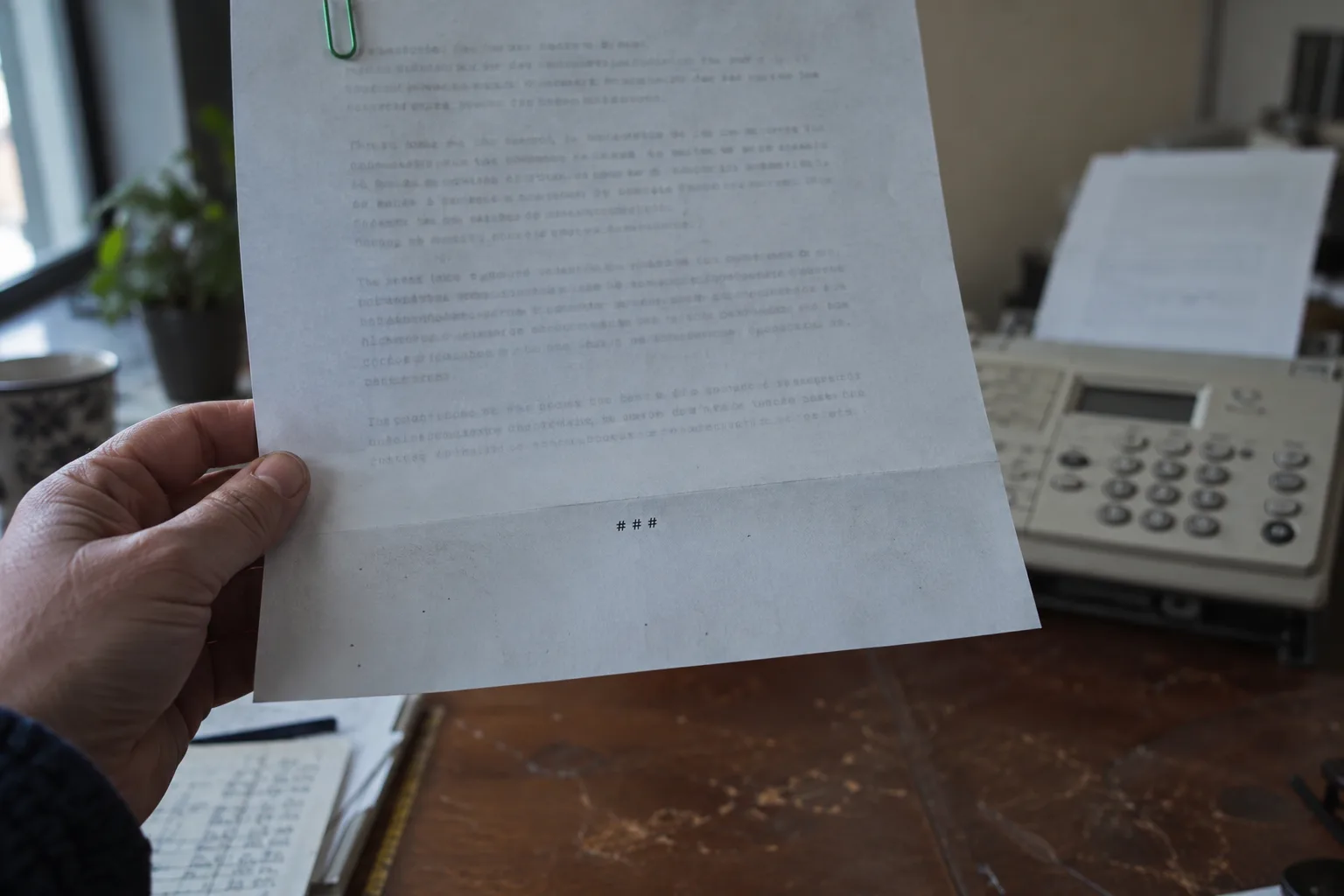 Hand holding the last page of a press release with the end mark centred, a fax machine behind